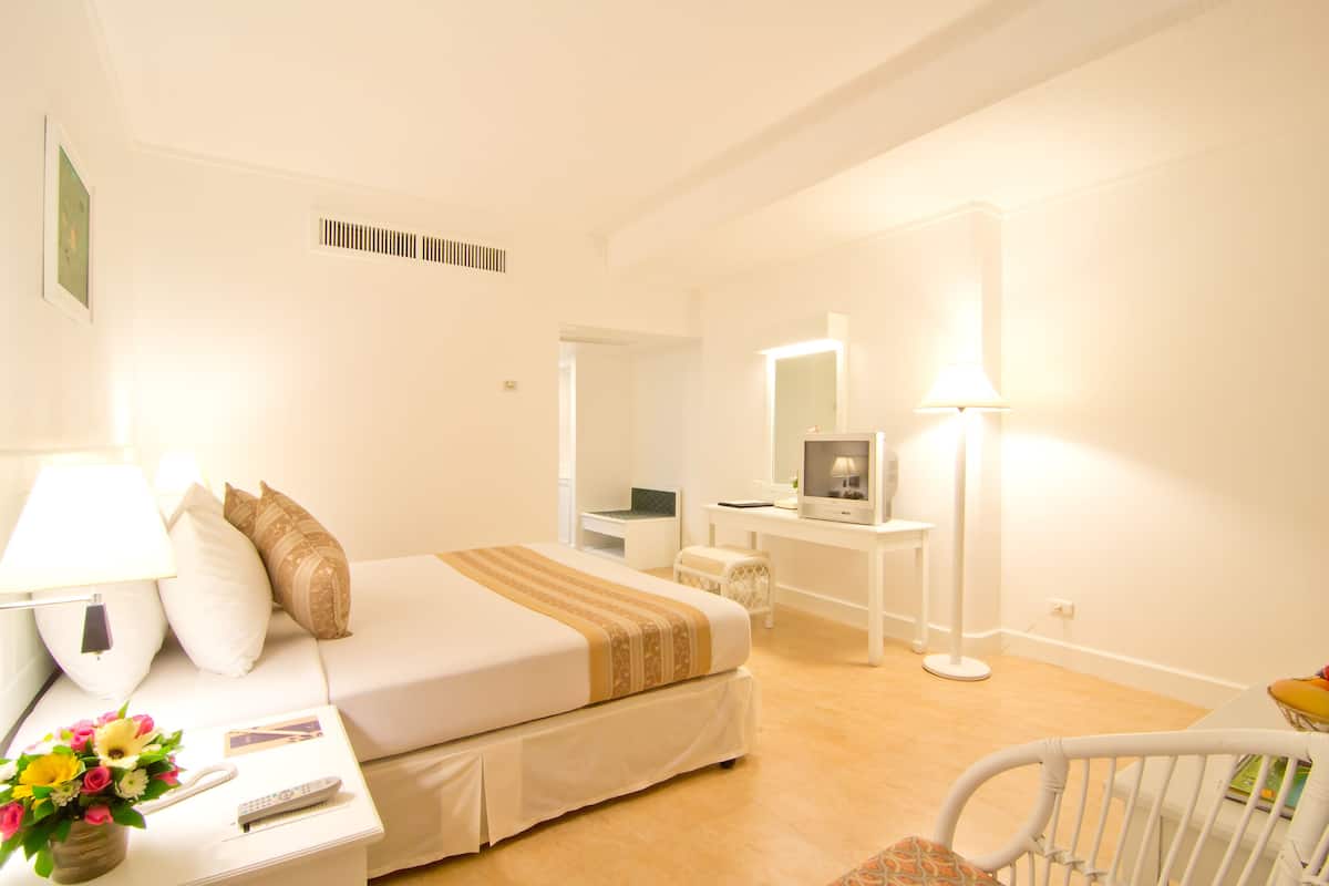 A hotel room with a bed, bedside table with a lamp, a chair, a desk with a computer, and a mirror.