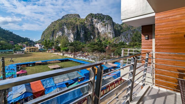 A balcony with a view of a mountainous landscape, a pool area, and a building with a wooden facade. - Coral Cliff Hotel (El Nido)