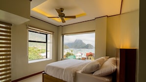 A bedroom with a bed, large windows, and a ceiling fan. - Coral Cliff Hotel (El Nido)