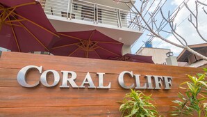 A wooden sign with "CORAL CLIFF" in large letters, surrounded by potted plants. - Coral Cliff Hotel (El Nido)