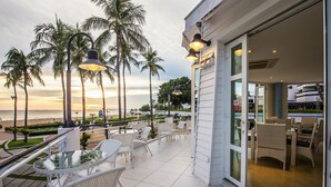 A balcony with white wicker furniture, a glass table, and a view of the beach and palm trees. - Ambassador City Jomtien Pattaya - Ocean Wing (Sattahip)
