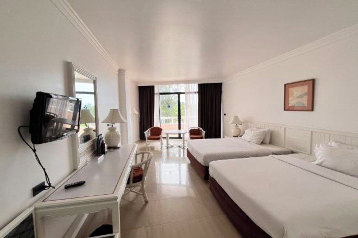 Habitación de hotel con dos camas, un escritorio, un televisor, una silla y una ventana con cortinas.