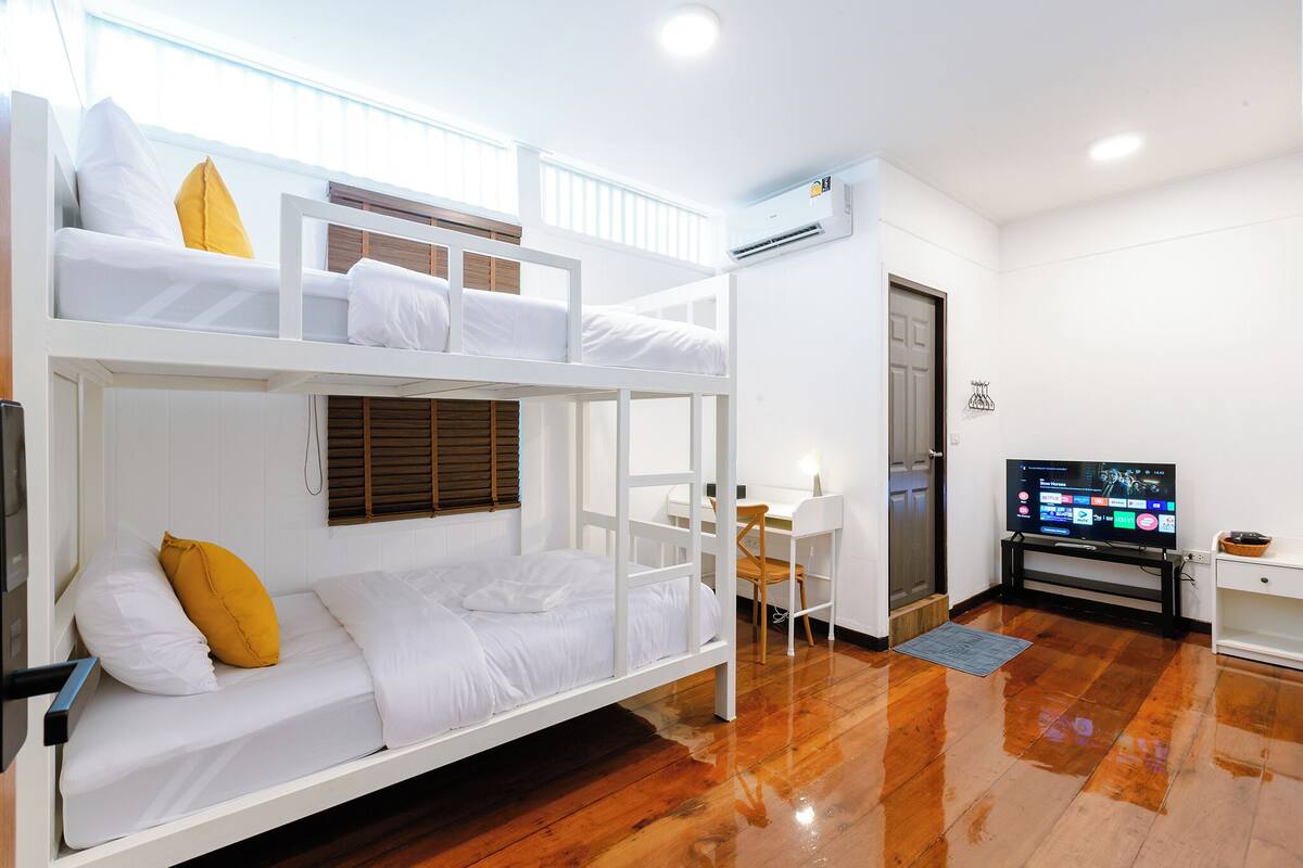Quarto com beliche, escrivaninha, televisão, piso de madeira e uma porta.