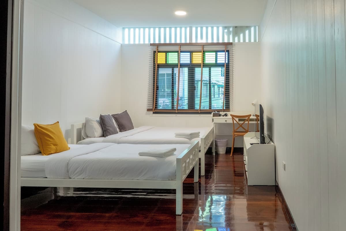 Quarto com duas camas, uma mesa e janela com cortinas.