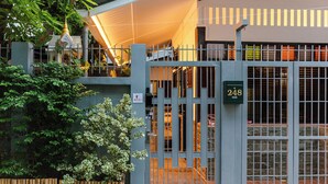 Une entrée fermée par un portail, surmontée d’un panneau indiquant un numéro, un petit sanctuaire et un arbre.