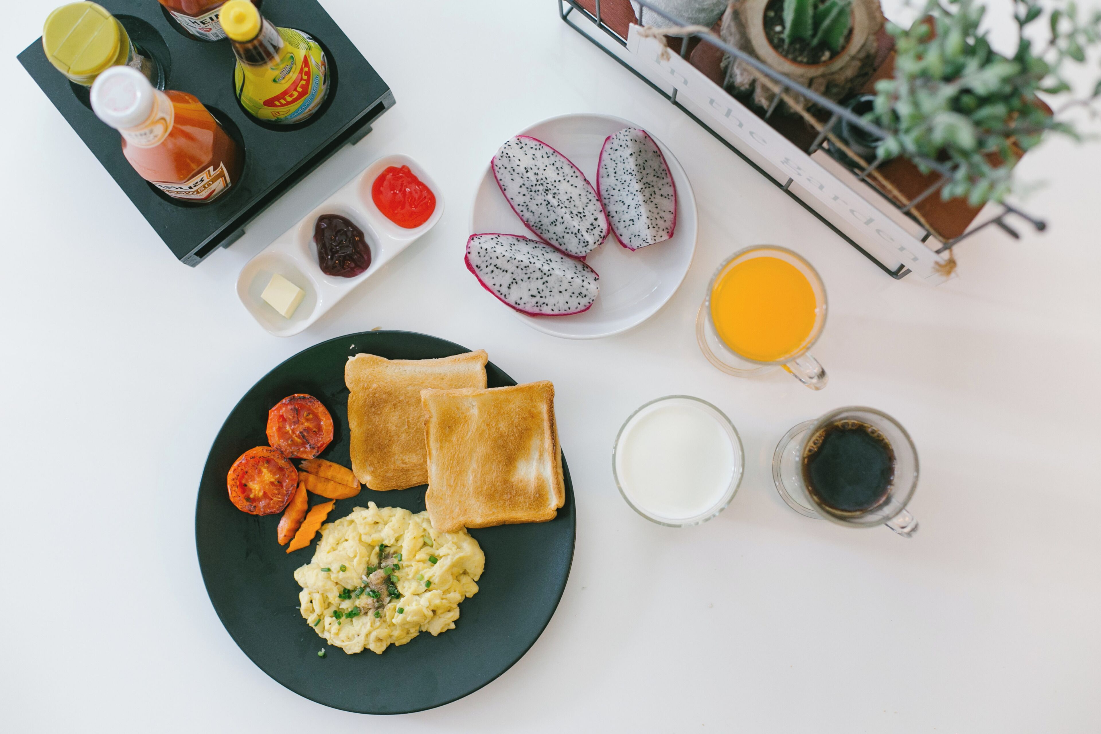 A breakfast setting with toast, scrambled eggs, tomatoes, and a plate of dragon fruit.