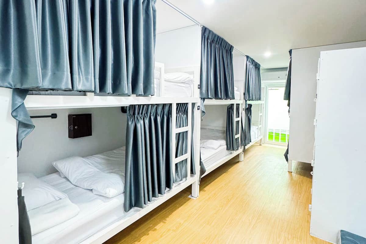 Quarto em dormitório com beliches, um ventilador e janela.