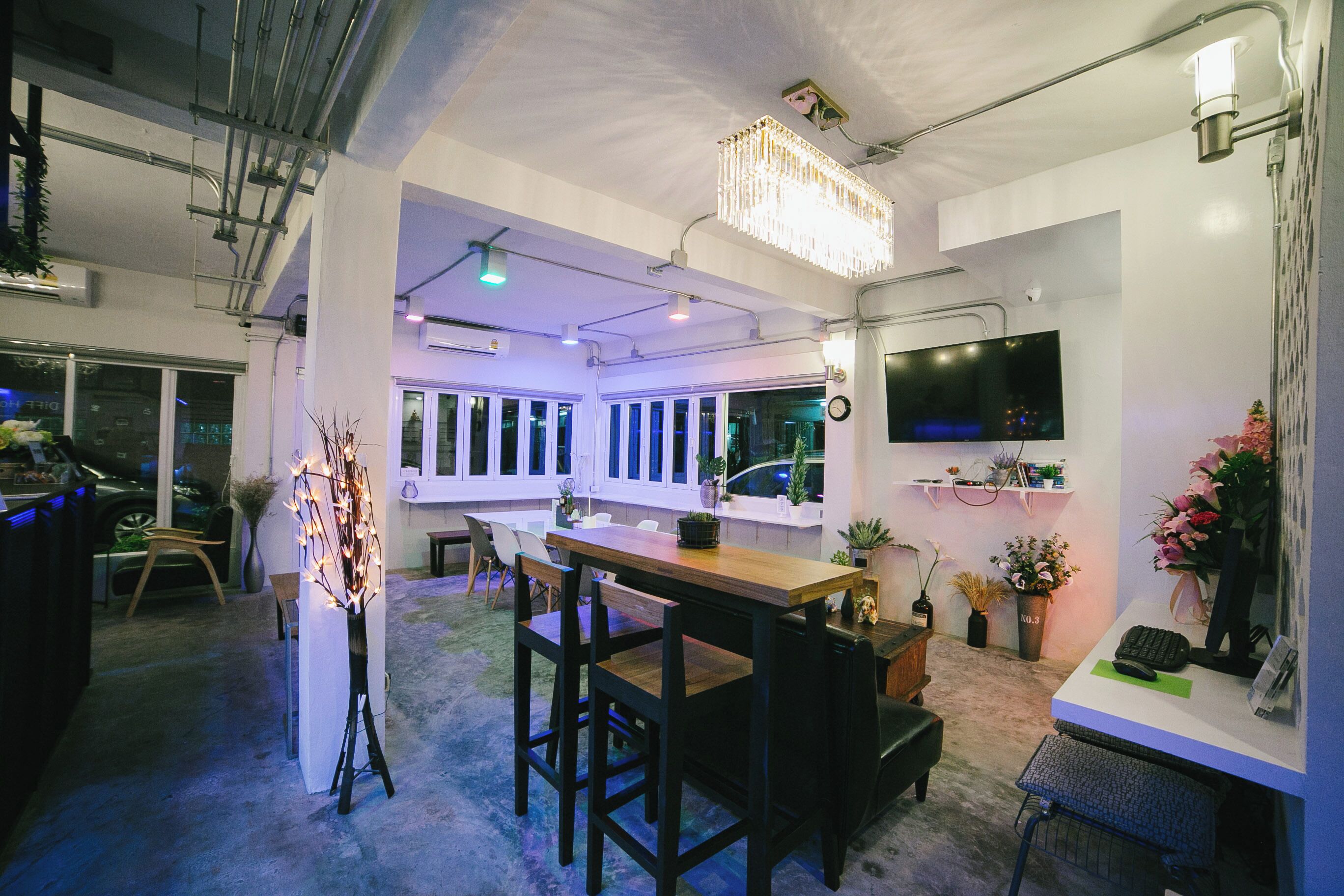A modern interior with a bar area, seating, a chandelier, and a TV mounted on the wall.