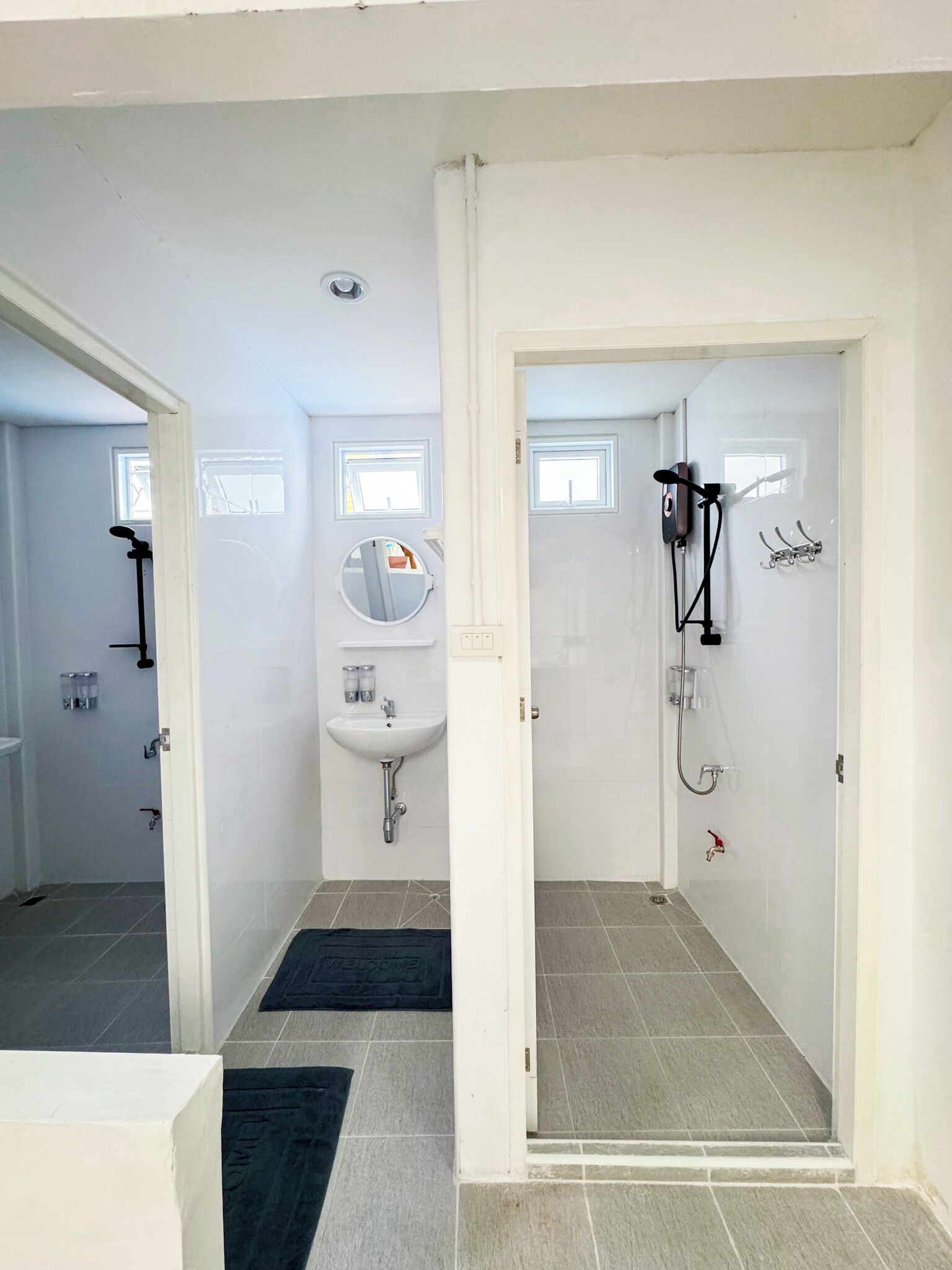 Une salle de bain avec un lavabo, un miroir et une douche. Elle comporte deux petites fenêtres et une porte qui donne sur une autre pièce.