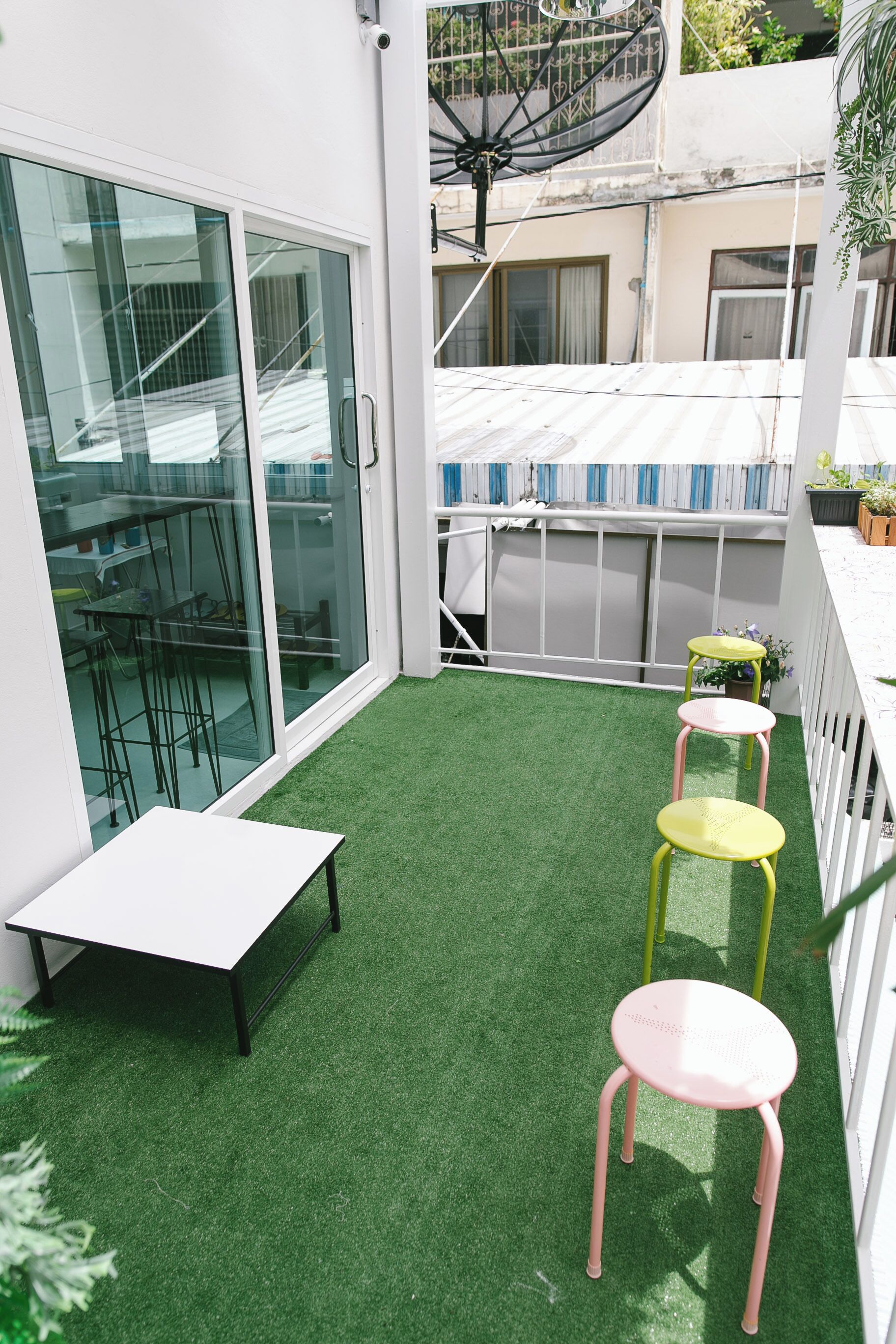 Un petit espace extérieur avec une pelouse artificielle, une table blanche et deux chaises.