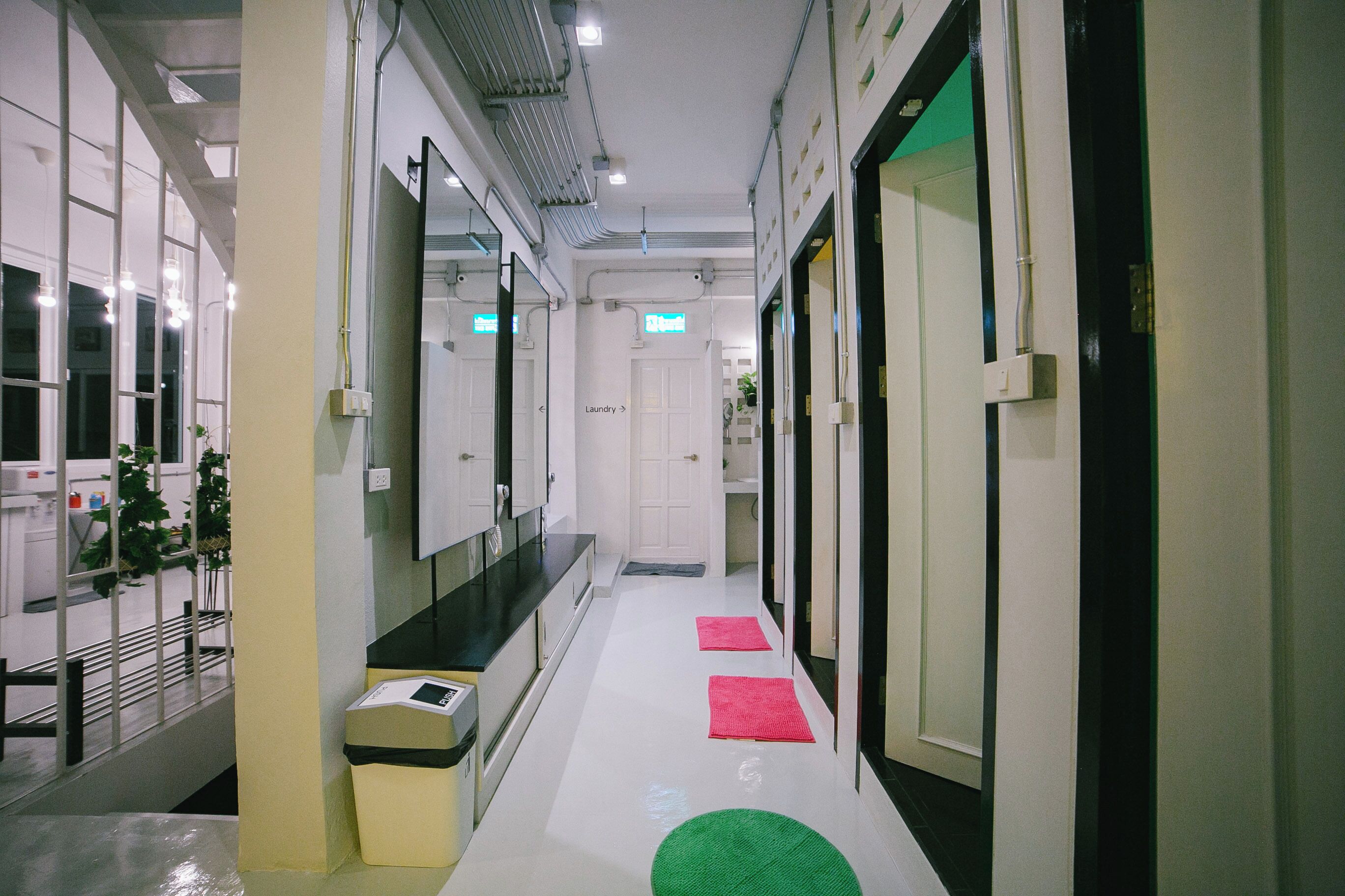 A hotel corridor with a white floor, a mirror on the left, a door labeled 'Laundry' in the center, and a green mat on the right.