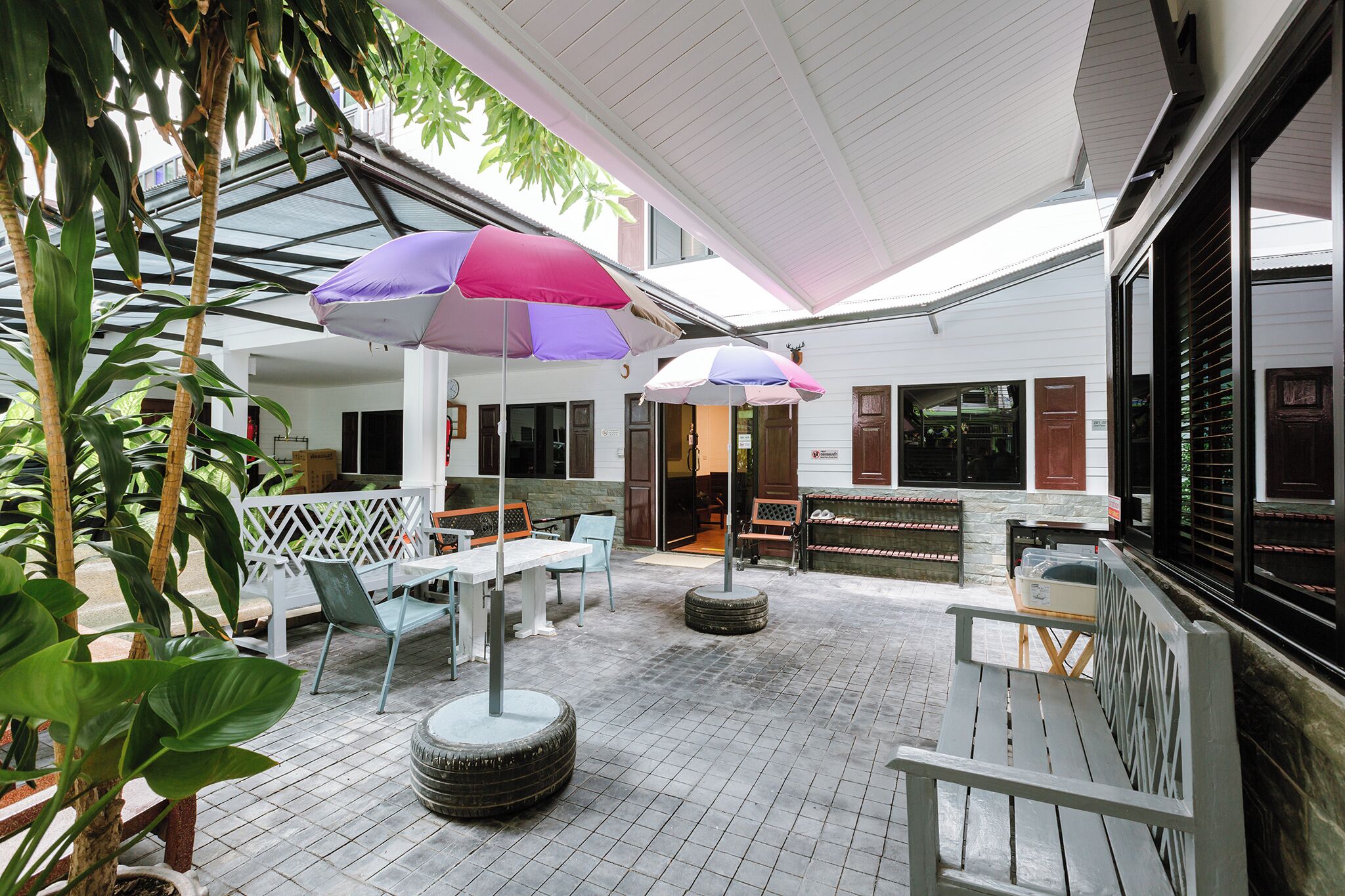 Ein Außenbereich mit Terrasse, Tischen und Stühlen, der von Sonnenschirmen beschattet und von Kübelpflanzen umgeben ist.