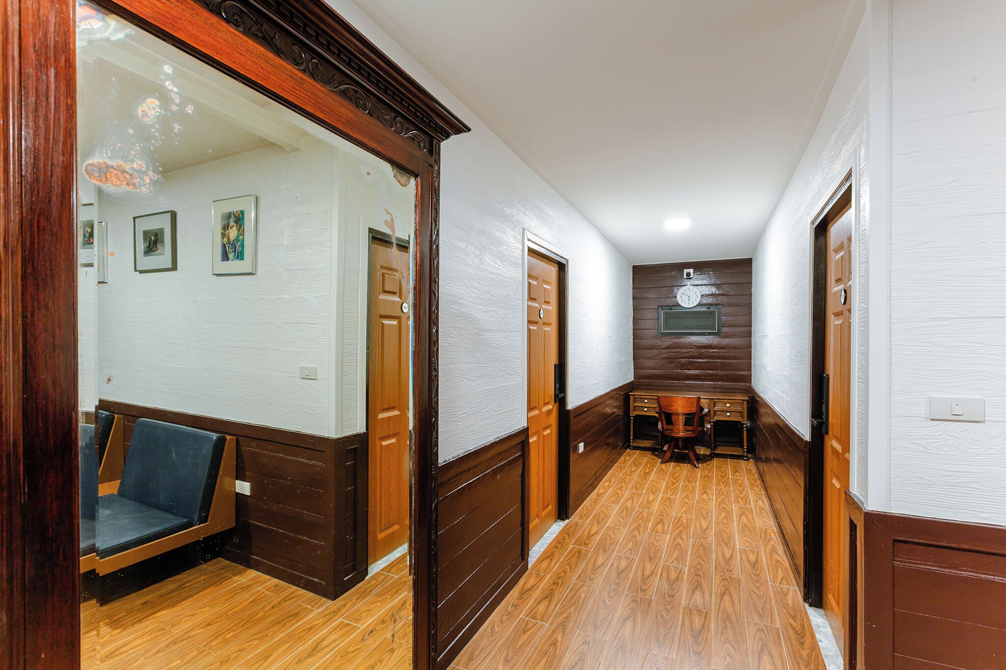 A hallway with wooden flooring, a bench, and a clock on the wall.