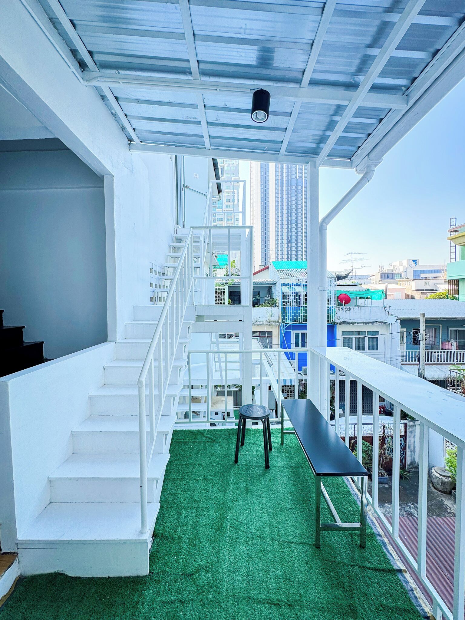 Un intérieur moderne avec des murs blancs, un sol recouvert d’un gazon artificiel vert, un banc noir et un escalier menant à un niveau supérieur.