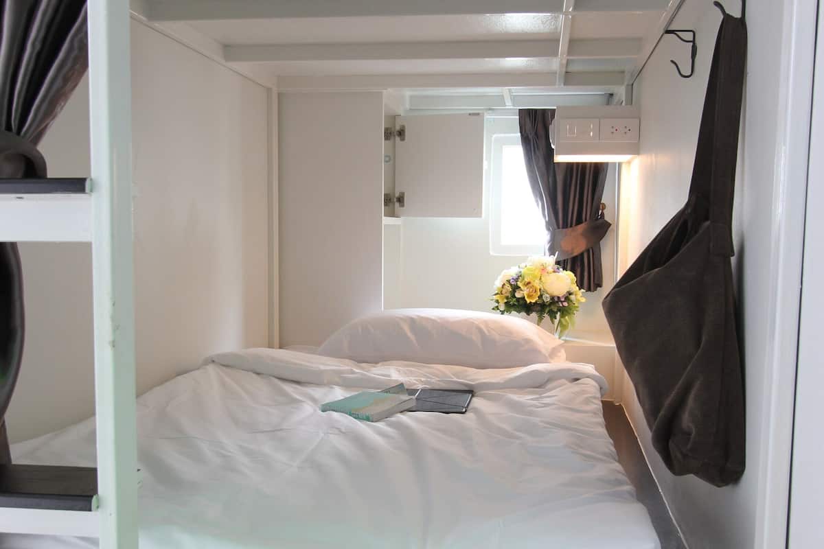 Uma cama beliche com roupa de cama branca, uma pequena mesa de cabeceira e um espelho sobre a cama.