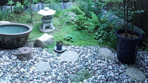A garden with a wooden fence, various plants, a stone lantern, and a large planter. - Guesthouse Chikayoshi (Kyoto)