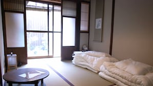A traditional Japanese room with tatami flooring, a futon bed, a small round table, and a shoji screen door. - Guesthouse Chikayoshi (Kyoto)