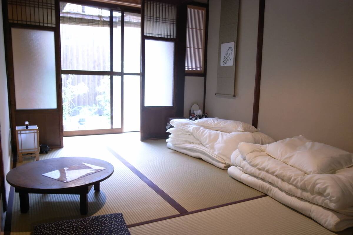 Una habitación japonesa tradicional con suelo de tatami, un futón, una pequeña mesa redonda y una puerta corredera de shoji.
