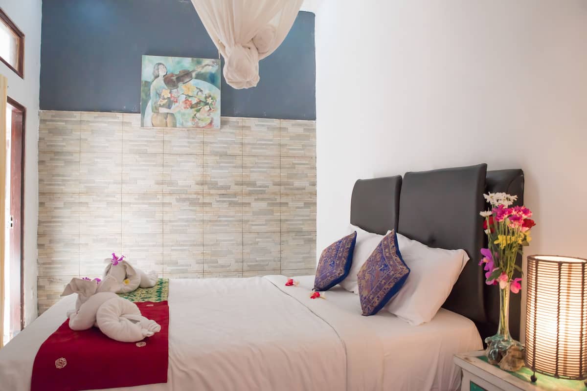 A hotel room with a bed, a nightstand with a lamp, a painting on the wall, and a window with curtains.