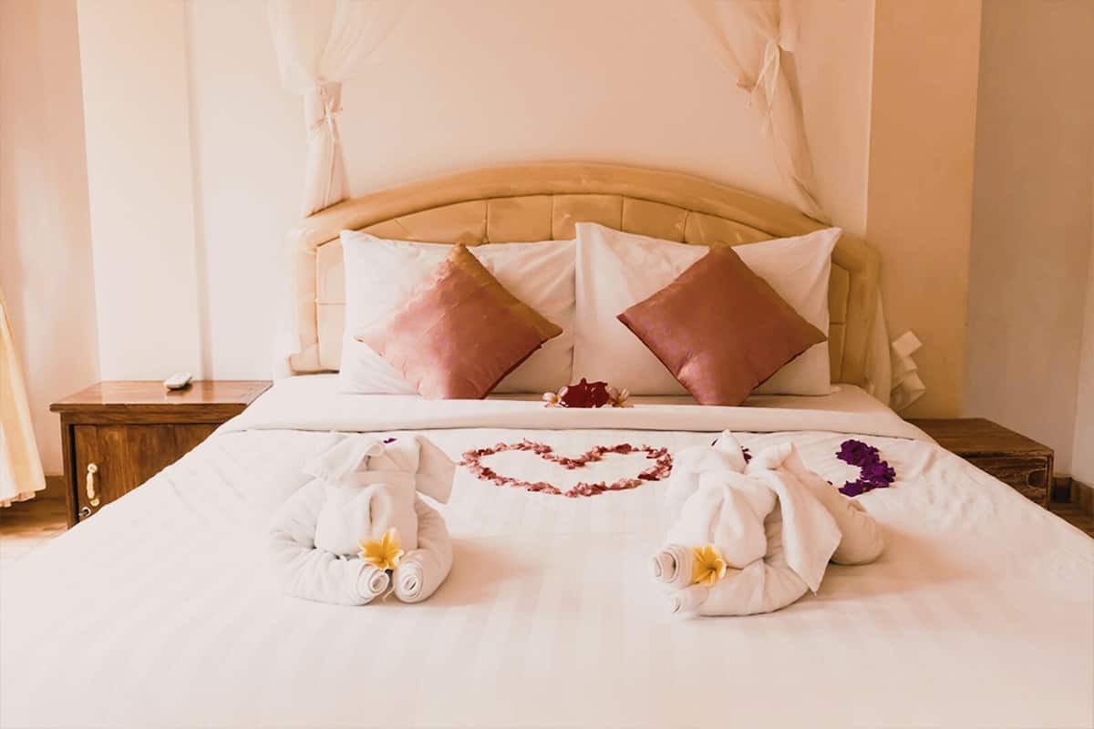 A neatly made bed with a heart-shaped towel arrangement, two pillows, and a bedside table with a remote control.