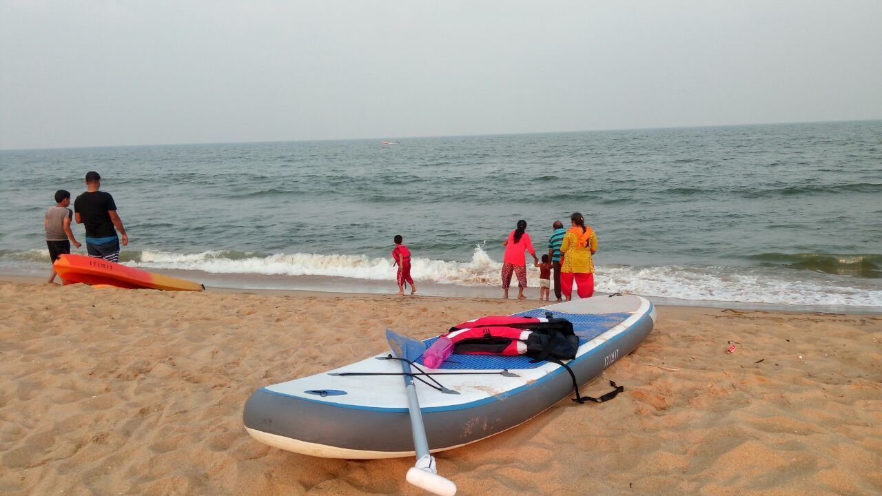 Ein Strand mit einem Stand-Up-Paddle und einem roten Kajak im Sand.