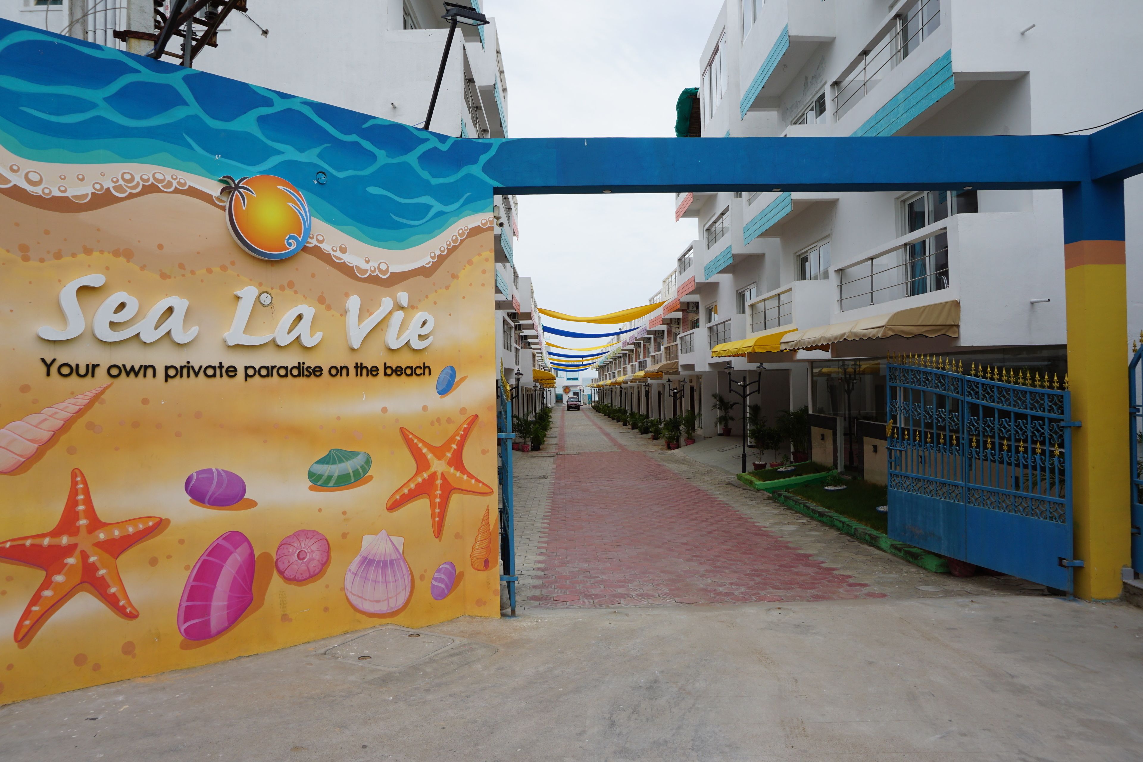 Un sentiero conduce a un edificio con un cartello colorato che recita 'Sea la vie' e un tema balneare.