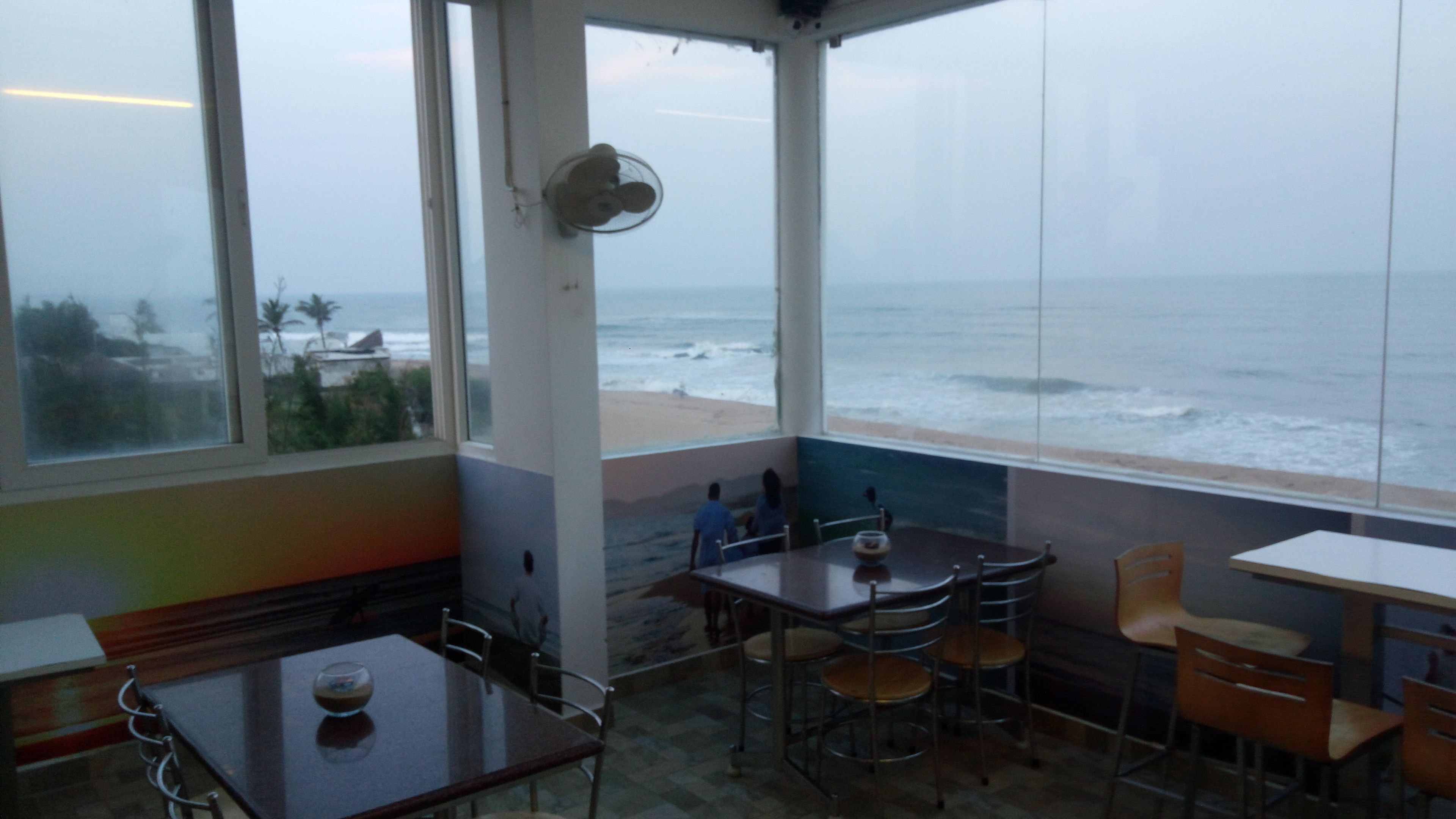 A room with a view of the ocean, a fan, and a table with chairs.