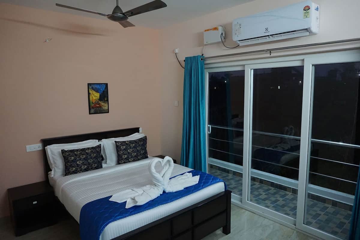 A bedroom with a bed, a ceiling fan, an air conditioning unit, a nightstand, a painting, and a sliding glass door.
