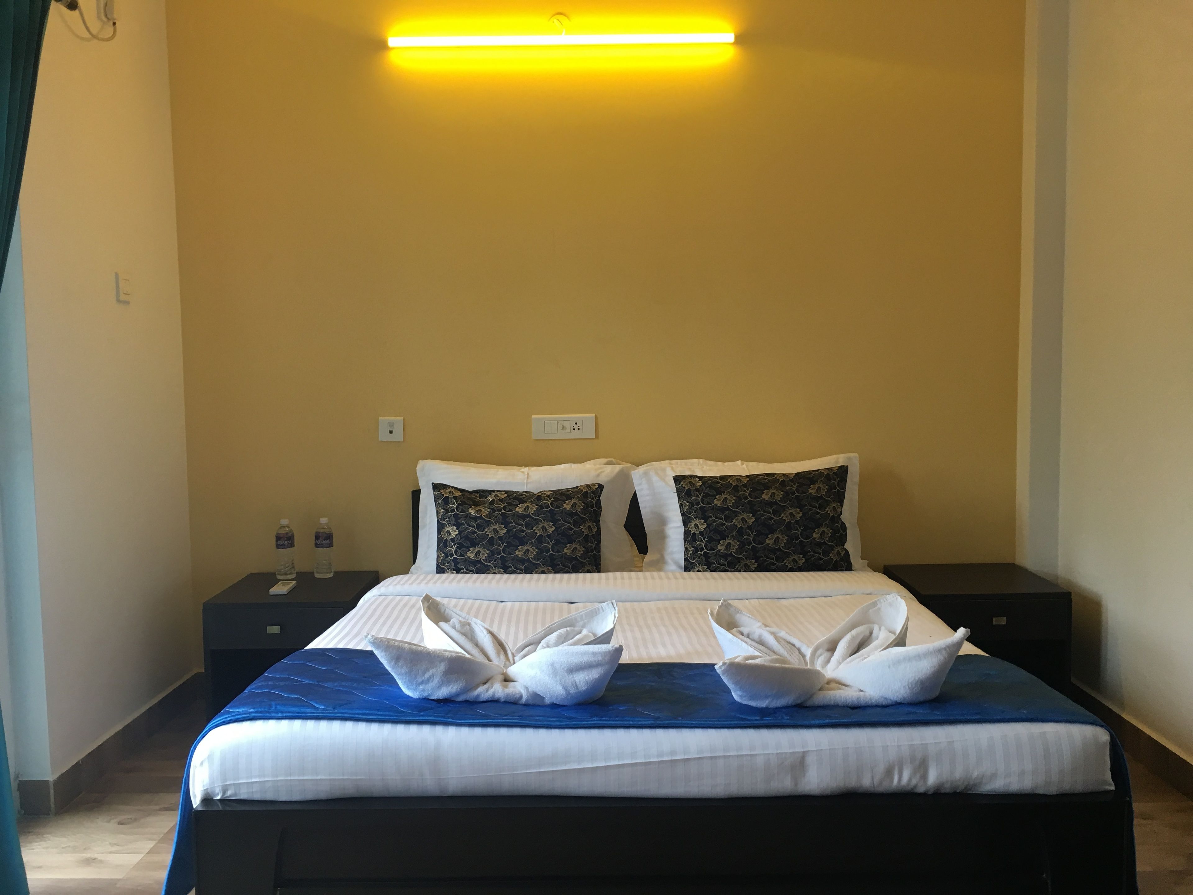 A hotel room with a bed, two nightstands, a water bottle, and a wall-mounted light.