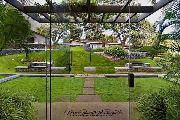 A glass-enclosed garden area with a stone pathway leading to a seating area, surrounded by lush greenery and a stone wall.