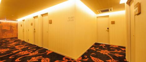A hotel hallway with multiple doors, a patterned carpet, and a sign indicating room numbers.