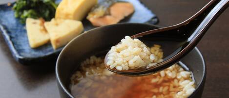 Un bol de riz, dont une cuillère de riz est soulevée, accompagné d’une assiette de nourriture en arrière-plan.