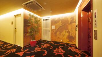 A hallway with a patterned carpet, a potted plant, and a wall with a mural.