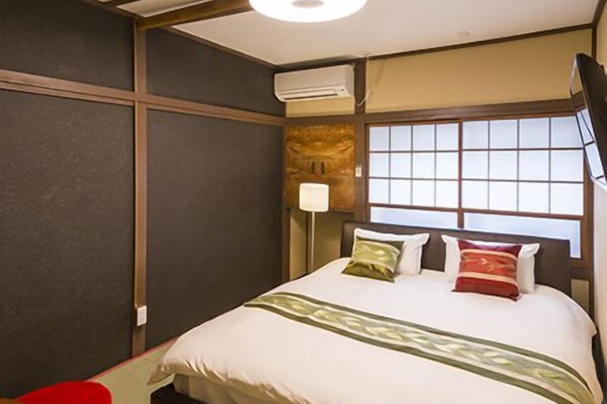 A hotel room with a bed, a red chair, a lamp, and a window.