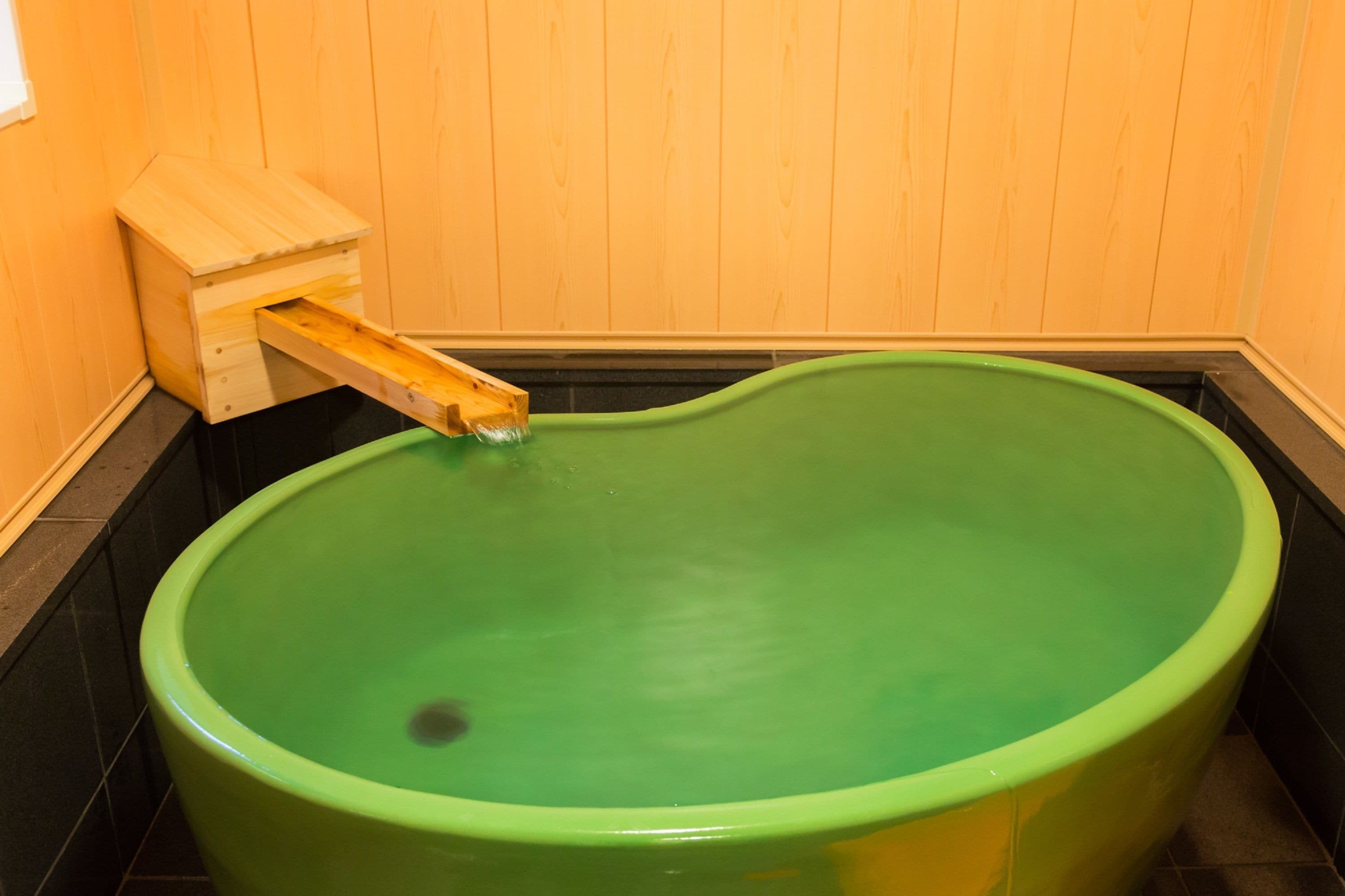 A green bathtub with a wooden structure attached to the wall.