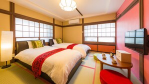 Habitación de hotel con dos camas, televisión, una mesa con un reloj y ventana con vistas.