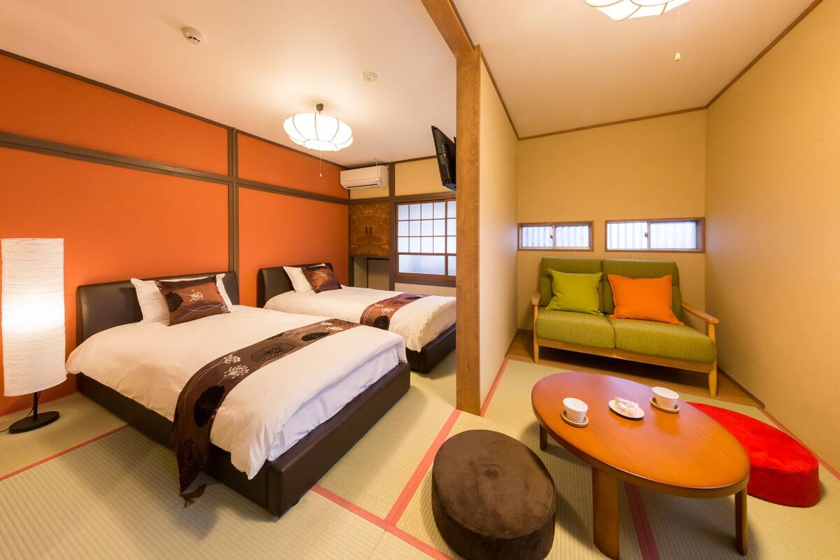A hotel room with two beds, a sofa, a small table with cups, and tatami mats.