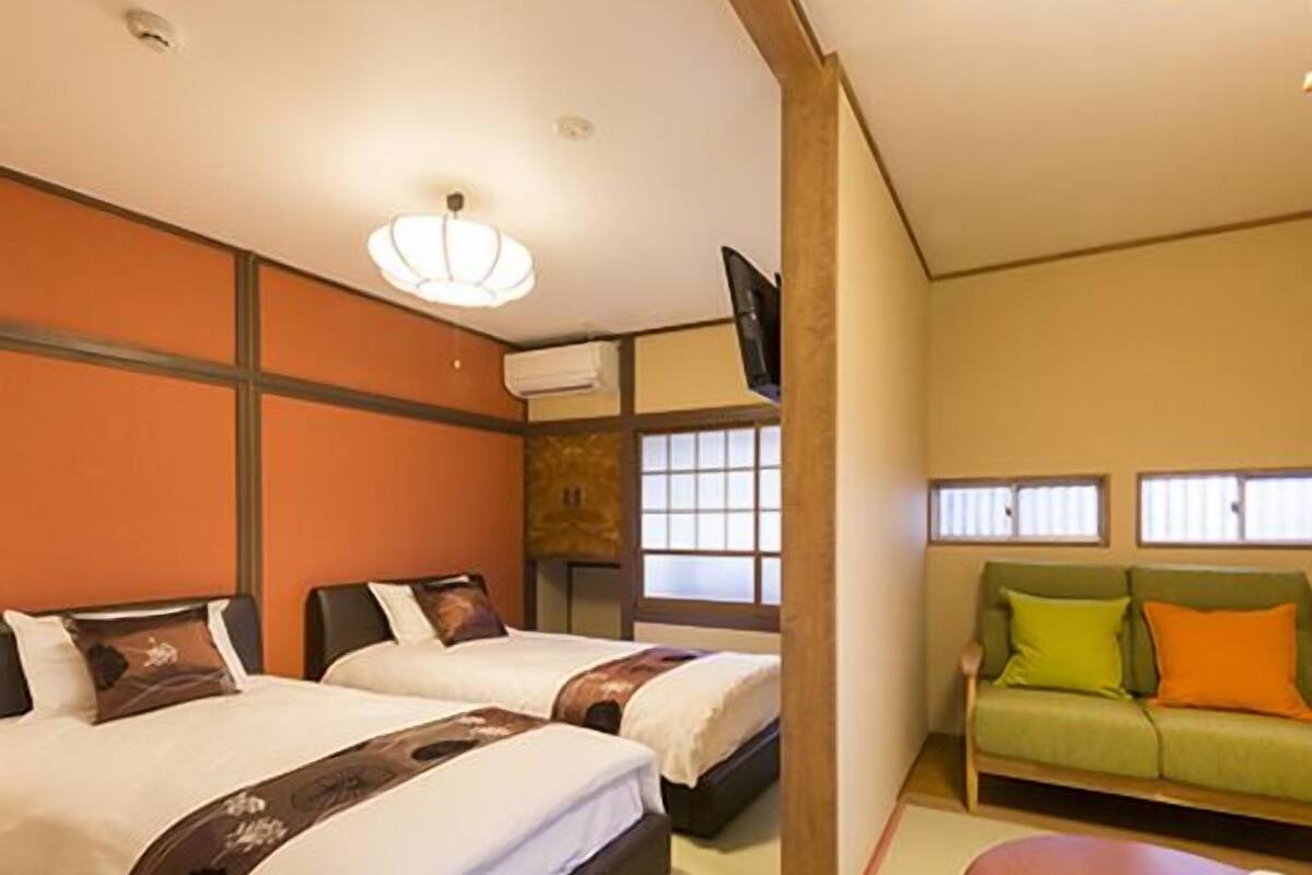 A hotel room with two beds, a sofa, a small table with cups, and a television.