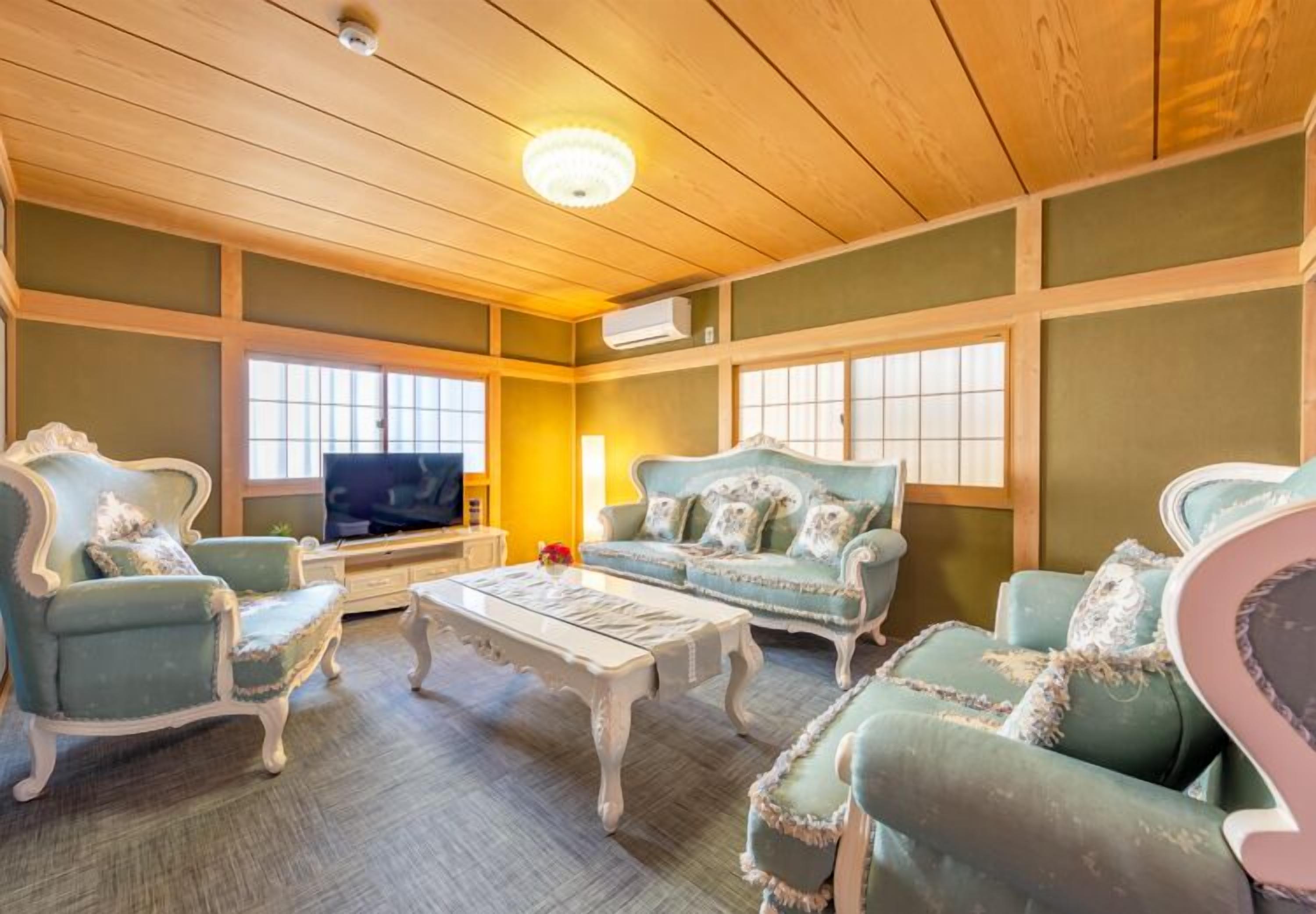A room with a wooden ceiling, a television, and two sofas with decorative pillows.