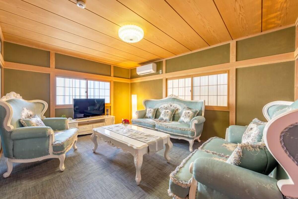 A room with a wooden ceiling, a television, and two sofas with decorative pillows.
