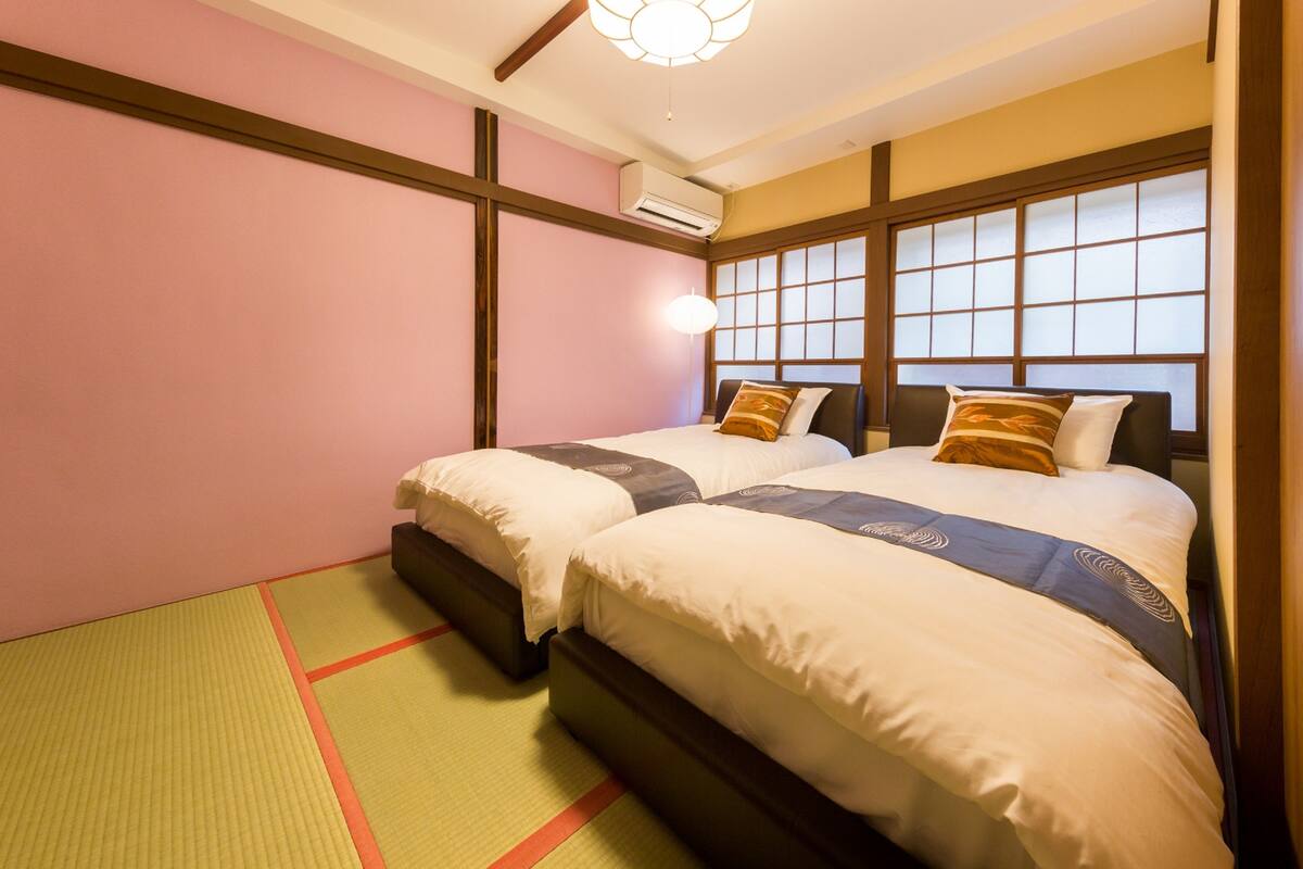 A hotel room with two beds, a traditional Japanese-style window, and tatami mats on the floor.