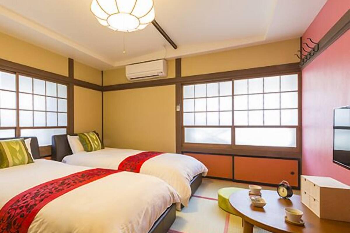 A hotel room with two beds, a small table with a clock, and a television on the wall.