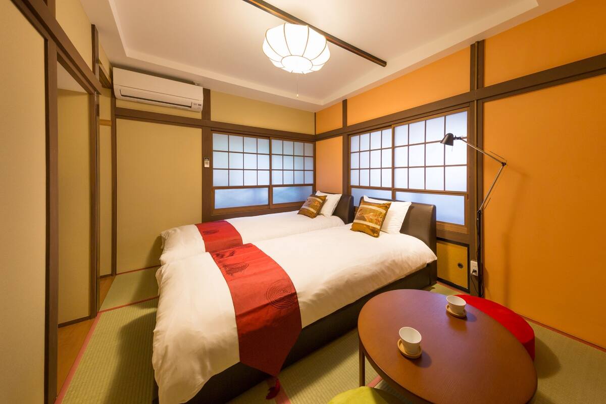 A hotel room with a bed, a table with two cups, and a lamp.