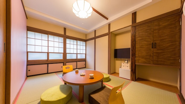 Una habitación japonesa tradicional con suelo de tatami, una mesa baja, cojines, puertas correderas y un televisor.