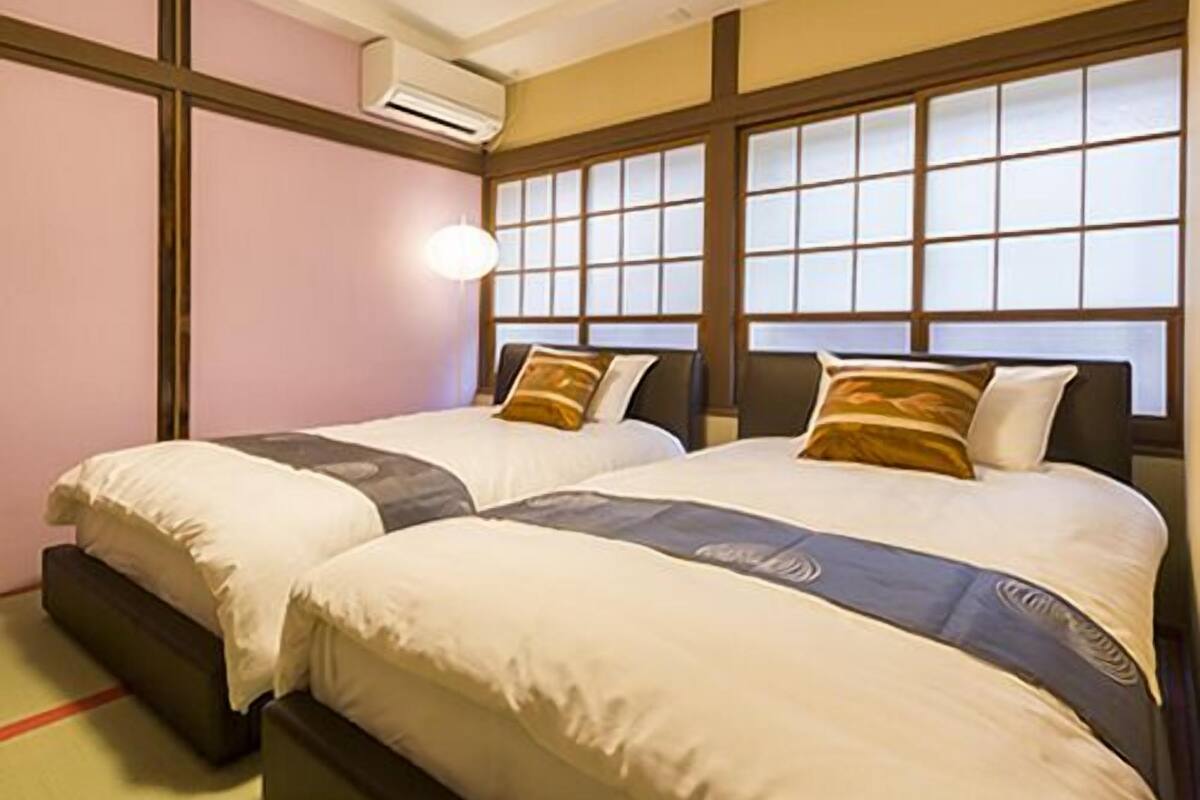 A hotel room with two beds, a large window with a view, and an air conditioning unit.