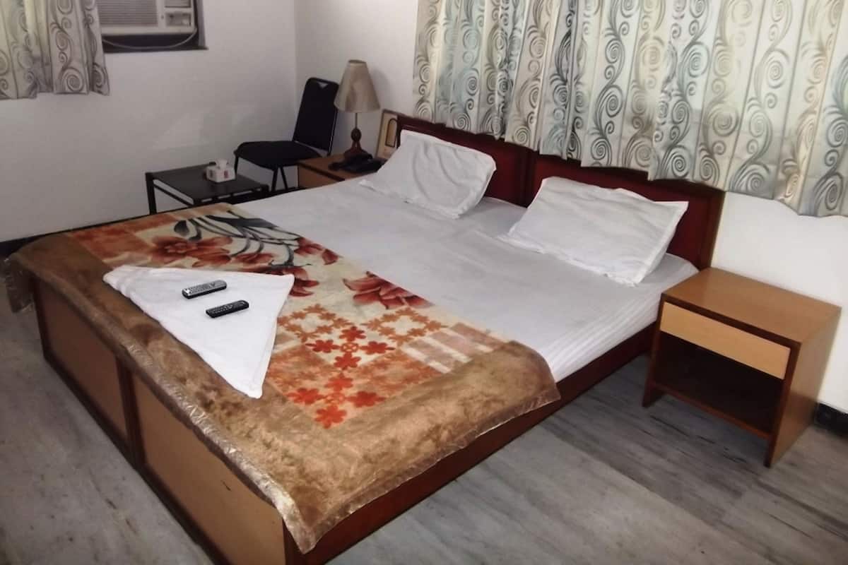 A hotel room with a bed, bedside table, chair, and an air conditioning unit.