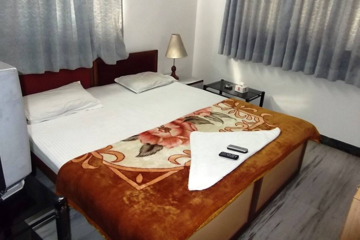 A hotel room with a bed, a nightstand, a lamp, and a window with curtains.