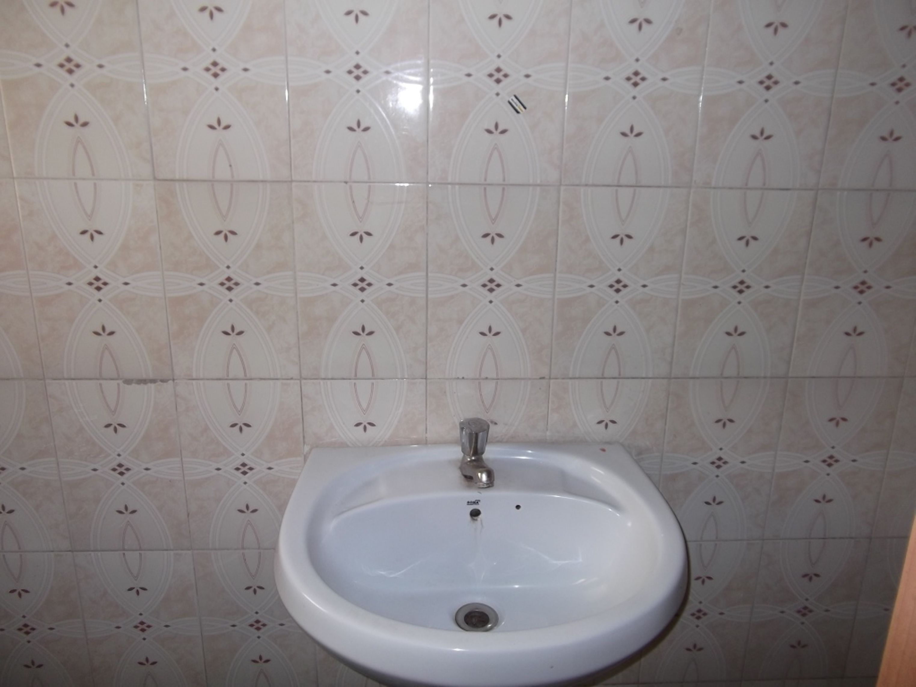 A bathroom with a white pedestal sink, tiled walls, and a drain.