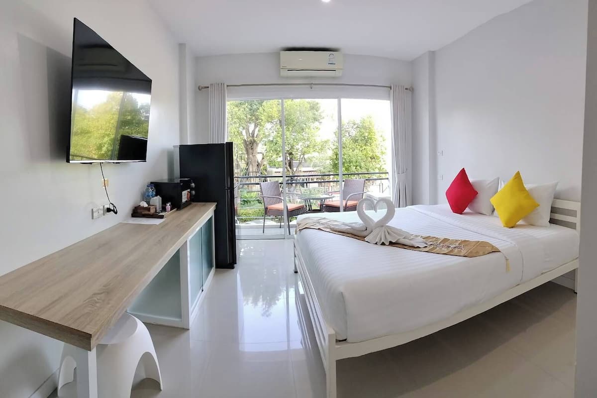 Habitación de hotel moderna con cama, escritorio, televisor y balcón con mobiliario exterior.