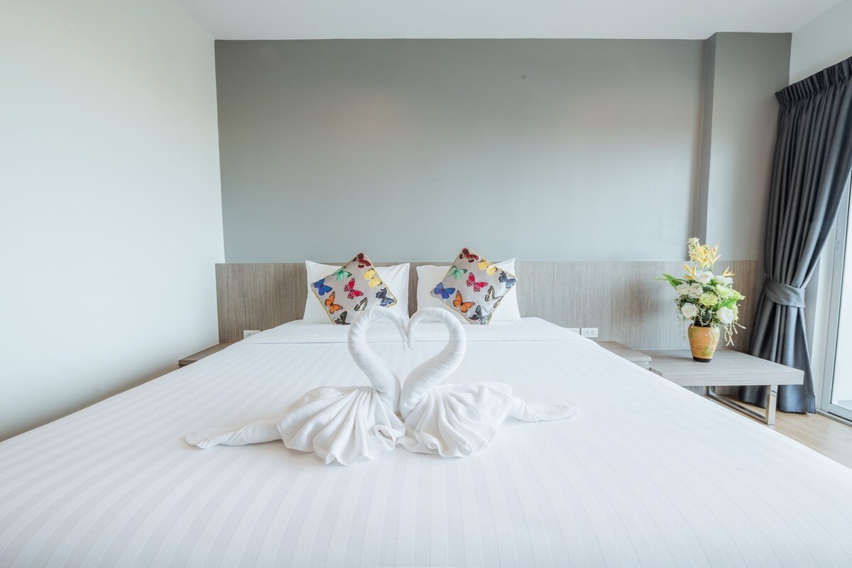 Une chambre d’hôtel avec un lit, des oreillers, un vase de fleurs et une fenêtre avec des rideaux.